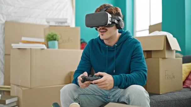 Nuori latino mies pelaa videopeliä käyttäen joystick ja virtuaalitodellisuus lasit uudessa kodissa - Materiaali, video