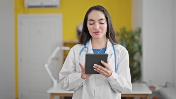Giovane bella donna ispanica medico sorridente fiducioso utilizzando touchpad presso la clinica - Filmati, video