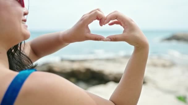 Młoda Chinka turystka w bikini robi gest serca nad morzem - Materiał filmowy, wideo