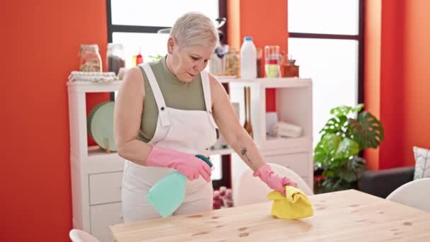 Mujer de pelo gris de mediana edad sonriendo mesa de lavado segura en el comedor - Metraje, vídeo