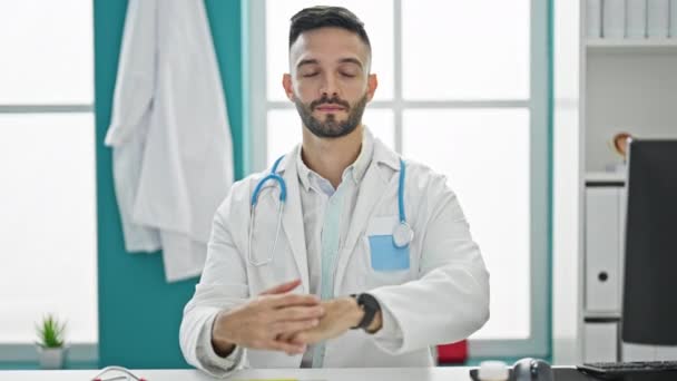 Giovane ispanico uomo medico seduto sul tavolo con espressione grave che punta a guardare la clinica - Filmati, video