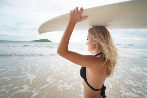 Сексуальна жінка позує з дошкою для серфінгу на пляжі. жінка несе над головою серфінг на заході сонця - Фото, зображення