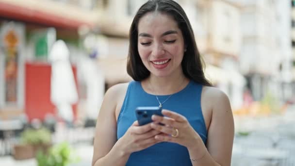 Joven hermosa mujer hispana usando smartphone celebrando en la calle - Imágenes, Vídeo