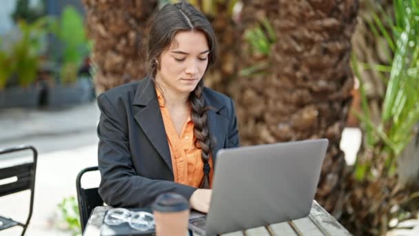 Nuori kaunis latino nainen liiketoiminnan työntekijä käyttäen kannettavaa tietokonetta hymyilee kahvilan terassilla - Materiaali, video