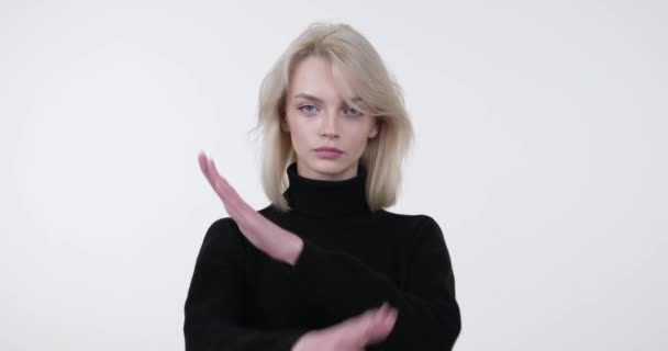Magabiztos kaukázusi nő áll szemben egy érintetlen fehér háttér. Megingathatatlan arckifejezéssel és határozott hozzáállással keresztbe teszi a karját egy erőteljes stop gesztussal.. - Felvétel, videó