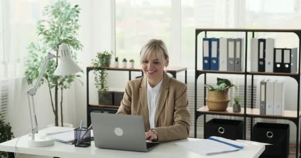 Šťastná obchodnice je viděna, jak pracuje se svým laptopem v kanceláři. Její radostná nálada a zářivý úsměv odrážejí její spokojenost s prací, kterou dělá. - Záběry, video