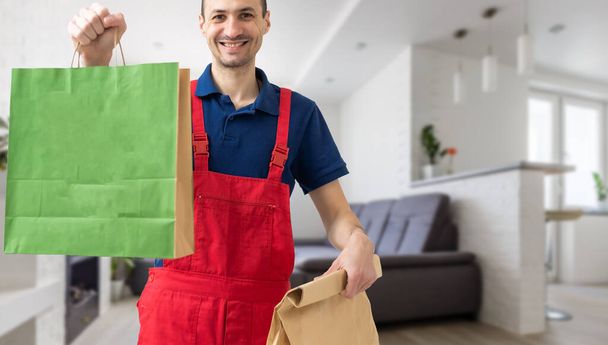Giovane uomo di consegna bello tenendo sacchetto di carta con cibo da asporto felice con grande sorriso - Foto, immagini