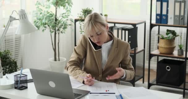 Žena manažerka multitasking, jak se zapojuje do telefonické konverzace při nakládání s papíry a dokumenty. Její výkonné a vyrovnané chování je důkazem její schopnosti zvládat pracovní povinnosti.. - Záběry, video