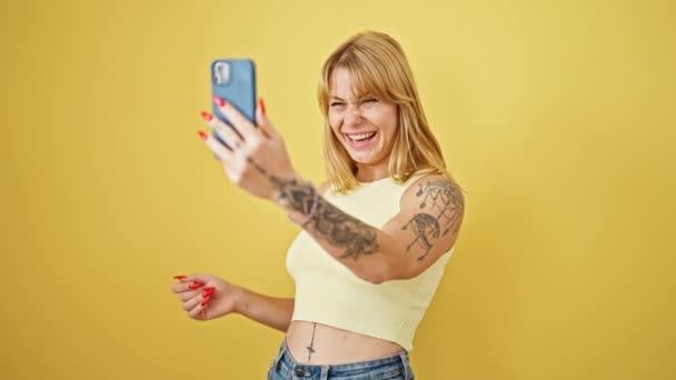 Joven mujer rubia sonriendo confiada teniendo videollamada sobre fondo amarillo aislado - Metraje, vídeo
