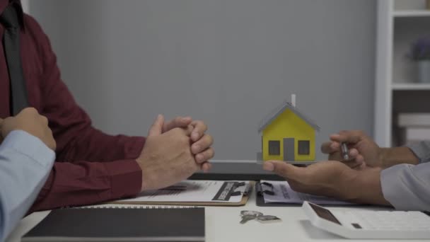 Immobilienmaklerin zeigt jungen asiatischen Paaren, die sich für den Kauf eines neuen Eigenheims interessieren, Hausdetails auf ihrer Akte und bietet Konditionen sowie die Unterzeichnung des Hauskaufvertrages und des Hausversicherungskonzepts - Filmmaterial, Video