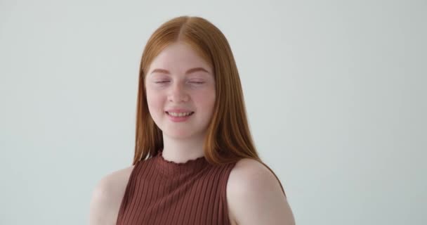 Une adolescente aux cheveux roux est capturée avec un sourire éclatant et un rire chaleureux sur un fond blanc. Son visage s'illumine de bonheur, et son vrai rire dégage un sentiment de joie et de positivité. - Séquence, vidéo