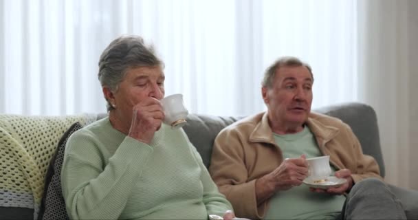 Coppia anziana, amici e bere tè e parlare sul divano o rilassarsi insieme in pensione e incontri sociali in soggiorno. Anziani, donne o uomini che parlano con il caffè e legano nella casa di cura. - Filmati, video