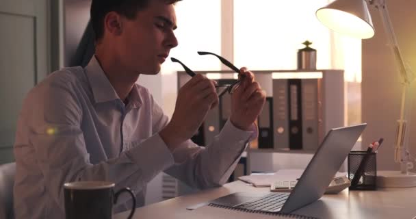 Focused businessman works on laptop. His fingers move across the keyboard, showcasing efficiency and dedication to the task at hand. Amidst work, he takes a moment to clean his glasses. - Metraje, vídeo