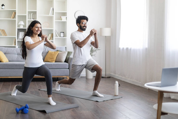 Evde antrenman. Spor yapan Hintli çift laptopun önünde kalça egzersizi yapıyor, mutlu genç doğu eşleri online dersler izliyor ve oturma odasında egzersiz yapıyor, birlikte spor yapıyorlar. - Fotoğraf, Görsel