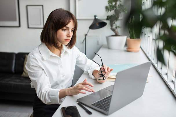 Focused confident businesswoman looking at laptop, create idea in office interior, free space. Planning business on gadget, problems in startup, work - Photo, Image
