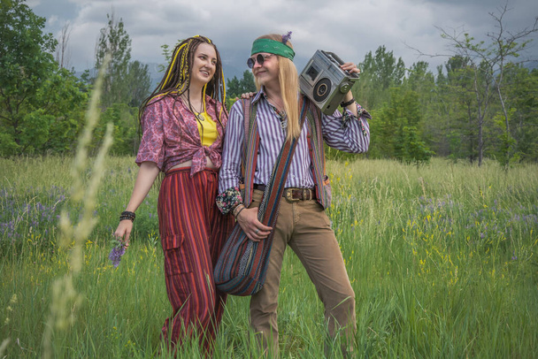 Hippie guy and girl listen to music on a vintage cassette recorder in a forest clearing - Photo, Image