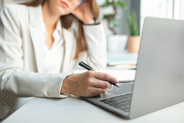 Empresária europeia pensativa em uso formal segurando caneta, sentada na frente do laptop no interior do escritório, foco seletivo, close-up. Reunião remotamente, trabalho, videochamada, negócios em gadget - Foto, Imagem