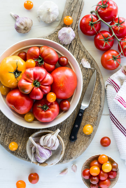 素朴な木製ボードにさまざまな新鮮な熟したトマトがいっぱいのボウル.  - 写真・画像