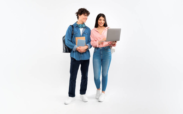 Электронное обучение, онлайн колледжное образование. Счастливые ученики, пользуясь топом, изучают дистанционно, стоя с рюкзаком и книгами на белом фоне. Молодые люди дружат по интернету - Фото, изображение