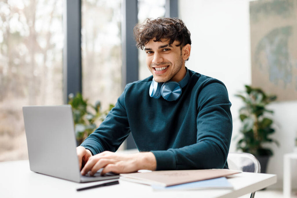 Портрет щасливого європейця, який посміхається на камеру, використовуючи ноутбук, сидячи в коворкінгу, вивчаючи дистанційно, переглядаючи вебінар, спілкуючись у віртуальному конференц-чаті, фрілансер насолоджується навчанням - Фото, зображення