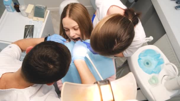 Два врача в защитных масках в стоматологической клинике, обслуживают пациентку. Здравоохранение и медицина. Вертикальное видео - Кадры, видео