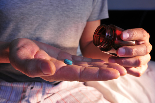 hombre en la cama a punto de tomar una píldora azul
 - Foto, Imagen