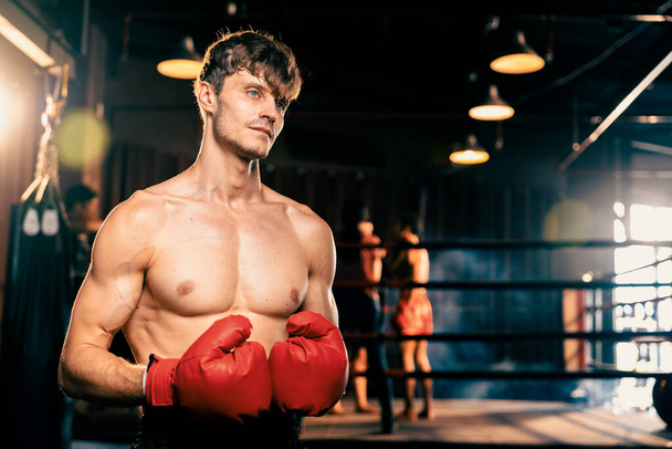 Boxing fighter shirtless posing, caucasian man boxer wearing red glove in defensive guard stance ready to fight and punch at gym with ring and boxing equipment in background. Impetus - Photo, Image