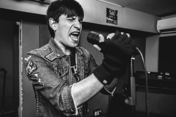 Vášnivý a intenzivní mladý rocker zpěvák uvolňující surovou energii během intenzivního metalového vystoupení ve zkušebně (v černobílé) - Fotografie, Obrázek