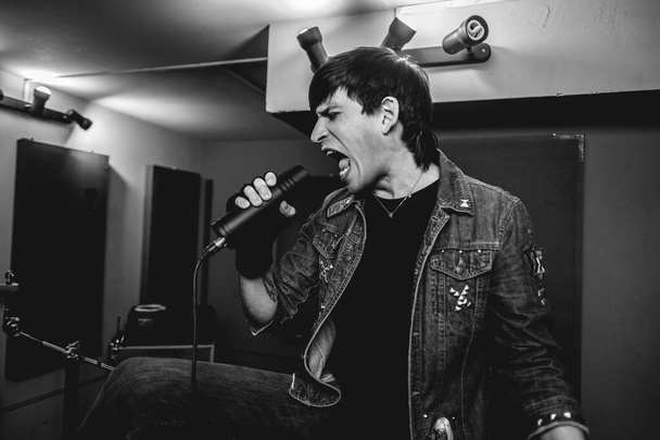 Passionate and intense young rocker vocalist unleashing raw energy during intense metal performance in a rehearsal room (in black and white) - Photo, Image