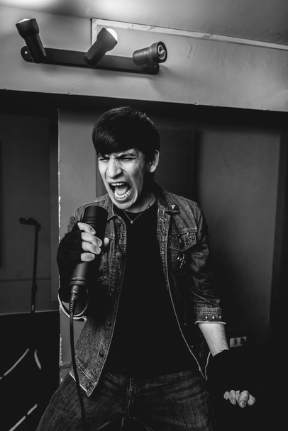 Szenvedélyes és intenzív fiatal rocker énekes szabadjára engedve nyers energia alatt intenzív fém előadás egy próbateremben (fekete-fehér) - Fotó, kép