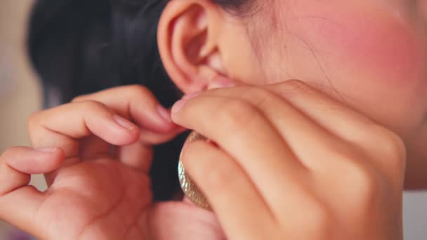 asijská žena nosí drahé zlaté náušnice v uších, zatímco se oblékají před zrcadlem v noci - Záběry, video