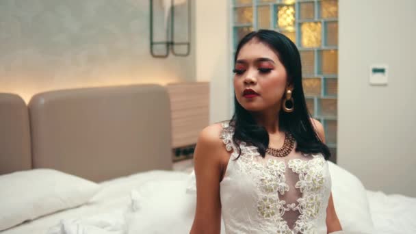 egy fehér ruhás ázsiai nő ül az ágyon, és szarkasztikusan néz a barátjára, miközben éjszaka egy szobában van. - Felvétel, videó