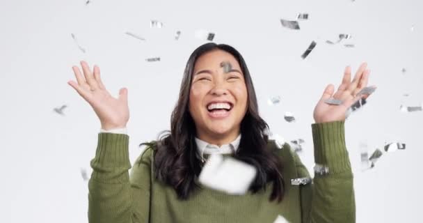 Happy asian woman, confetti and celebration in winning, promotion or achievement against a grey studio background. Portrait of excited female person smile in happiness for prize, party or victory. - Footage, Video