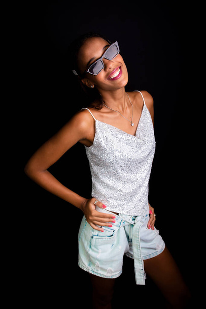 Hermosa chica adolescente posando para la foto en el estudio. Llevando gafas de sol. Aislado sobre fondo negro. - Foto, Imagen