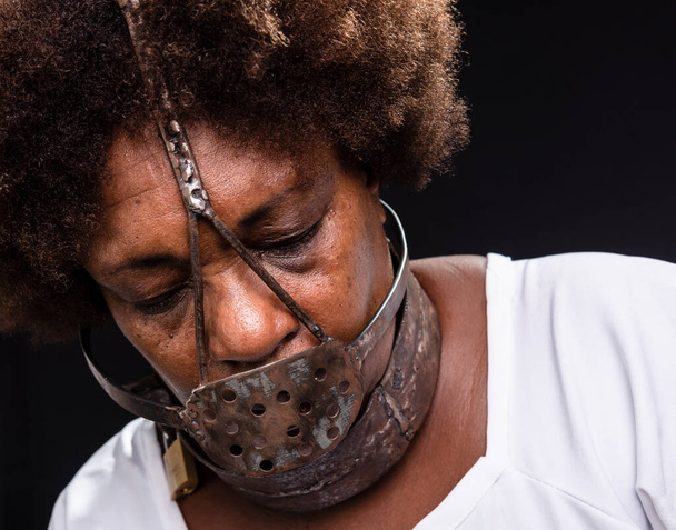 Portrét černé ženy s železnou maskou na tváři, představující otrokyni Anastacii. Bolest a utrpení, mučení. Na černém pozadí. - Fotografie, Obrázek