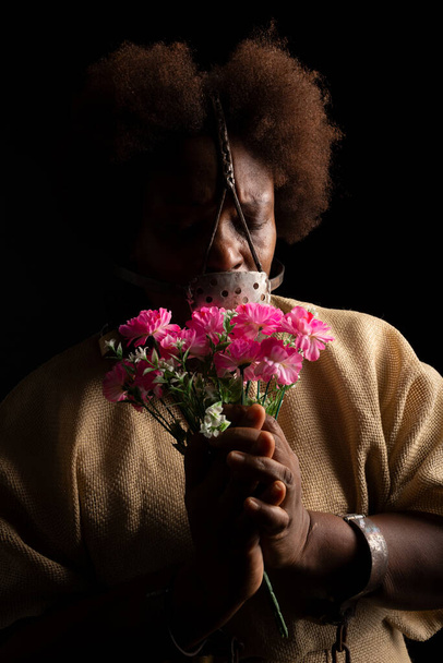 鎖を手にした黒人女性の肖像画と、花の束を手にした顔に鉄のマスク。アナスタシアを奴隷に。ブラジルにおける奴隷制. - 写真・画像