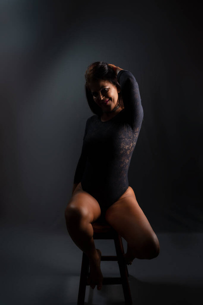 Studio portrait of beautiful sensual brunette model wearing black lingerie, sitting, making sexy poses. . Against dark background. - Φωτογραφία, εικόνα