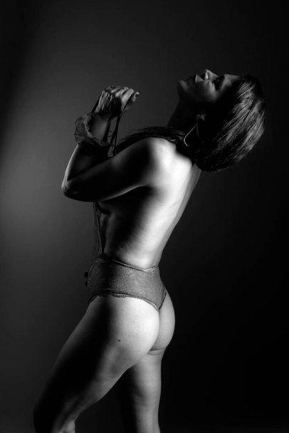 Černobílý portrét smyslného modelky ve spodním prádle, stojící, vytvářející sexy pózy. Fotka ze studia. Na tmavém pozadí. - Fotografie, Obrázek