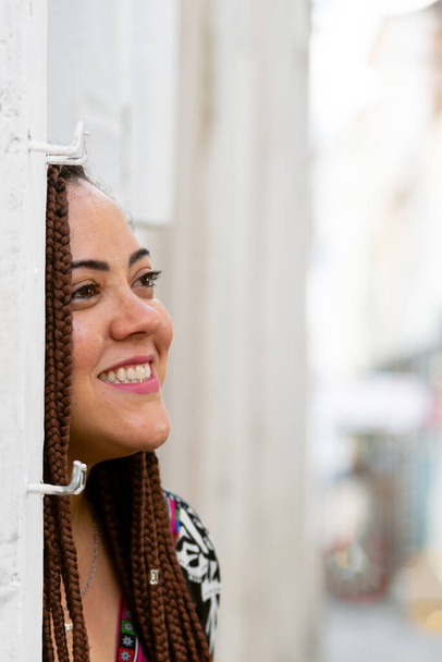 Tvář portrétu krásné ženy s copánky opřenými o zeď. Ulice v pozadí. Turista na výletě. Pelourinho, Brazílie. - Fotografie, Obrázek