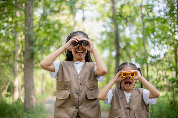 Happy Little Asian meisjes kijken vooruit en glimlachend kind met de verrekijker in het park. Reizen en avontuur concept. Vrijheid, vakantie - Foto, afbeelding