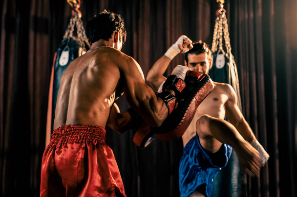 Le boxeur asiatique et caucasien Muay Thai déclenche une attaque de coups de pied dans une séance d'entraînement de boxe féroce, donnant un coup de pied à l'entraîneur sparring, mettant en valeur la technique et les compétences de boxe Muay Thai. Impulsion - Photo, image