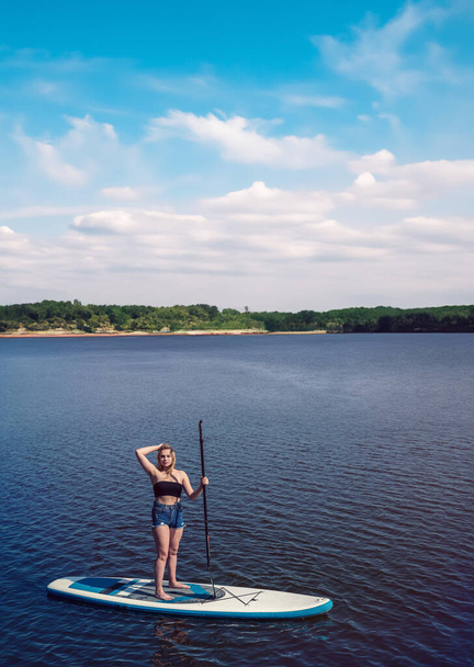 Jovem mulher magra no tempo de verão remando na placa SUP em belo lago, estilo de vida saudável - Foto, Imagem