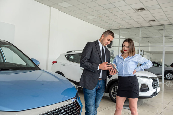  Beautiful client with salesman manager selling vehicle with tablet at car salon showroom  - Foto, imagen