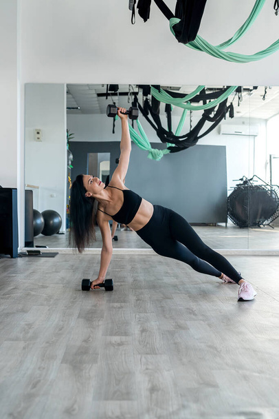 Νεαρή λεπτή γυναίκα κάνει άσκηση με αλτήρες στο γυμναστήριο. Ο αθλητισμός ως τρόπος ζωής - Φωτογραφία, εικόνα