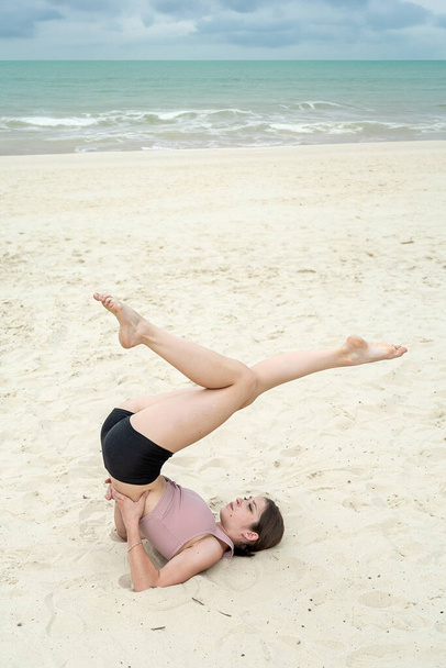 Mujer en ropa deportiva meditando en la playa de arena cerca del lago. Concepto de ejercicio de yoga o pilates al aire libre - Foto, imagen