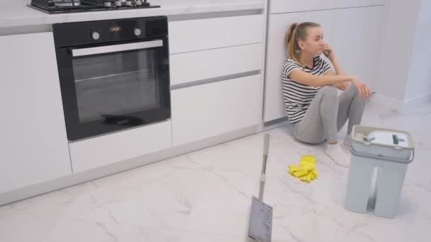 Unavená žena mluví po telefonu, když uklízí dům. Úklid podlahy v domě. - Záběry, video