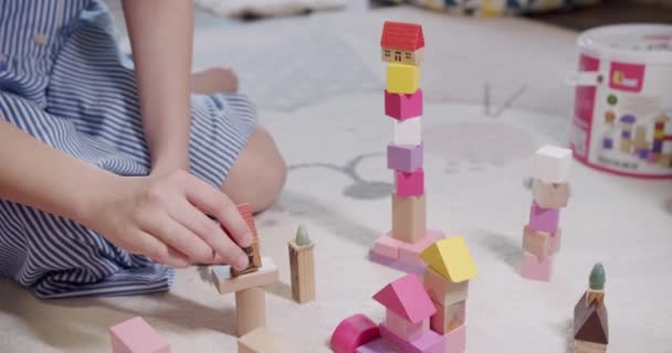 Kinderen spelen met speelgoed zitten thuis op vloerkleed. Kinderen bouwen toren van houten blokken. Geniet van het spel in de woonkamer. Kind spelen met houten bouwstenen. Geniet van spel activiteit - Video