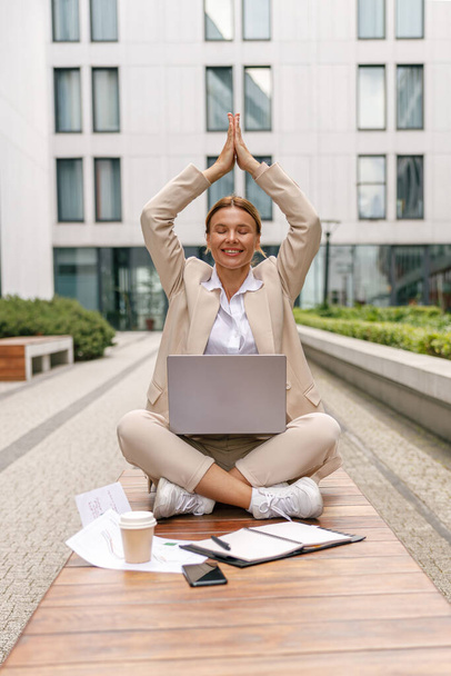 Directora mujer enfocada sentada en posición de loto y meditación durante el descanso con el trabajo en línea - Foto, imagen