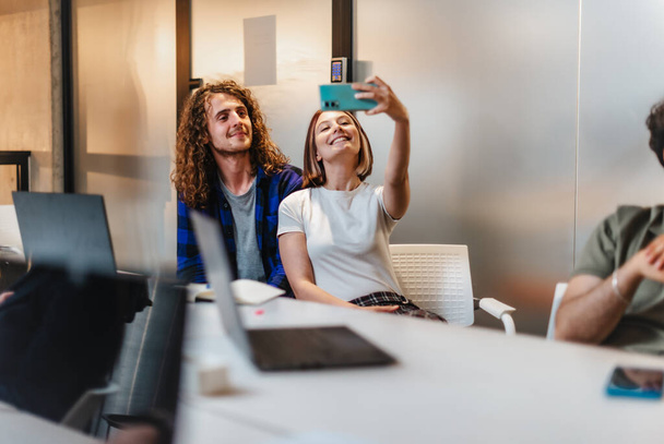 Belos e jovens funcionários se divertindo durante a pausa no trabalho, tirando uma selfie e sorrindo - Foto, Imagem