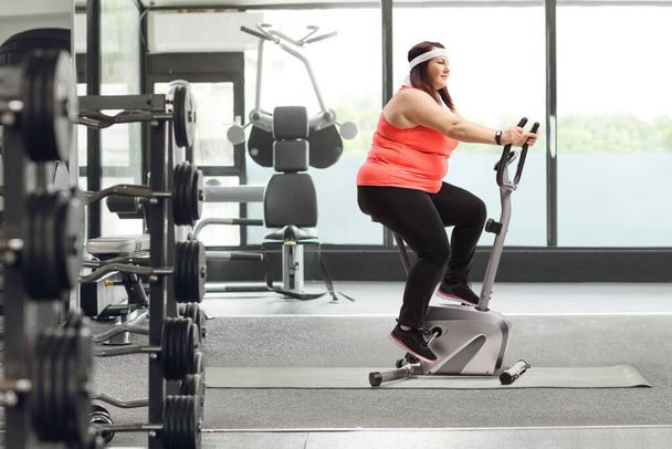Corpulent woman riding a stationary bike at the gym - 写真・画像